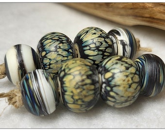 May include: A collection of handcrafted beads with unique patterns and colors. The beads are round, with a mix of black, white, blue, and yellow designs. They are strung together with natural twine, showcasing a rustic aesthetic.