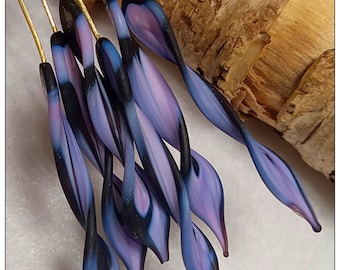 May include: Close-up of a collection of glass art pieces. Each piece features a slender, elongated shape with a gradient of colors, including shades of purple, blue, and black. The pieces are attached to thin, gold-colored wires, suggesting they are decorative items.
