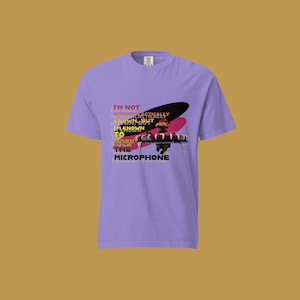 May include: Purple t-shirt with a graphic of a cartoon character holding a microphone. The text on the shirt reads "I'm not internationally known but I'm known to rock the microphone."