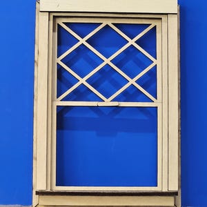 May include: A miniature wooden window with a diamond lattice design. The window frame is a light beige color, and the background is a vibrant blue. The window is a detailed craft item.