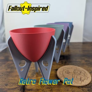 May include: A row of retro-style flower pots in red, green, purple, and blue, with gray supports. The pots are labeled "Fallout-Inspired" and "Retro Flower Pot." A round coaster with a thumbs-up graphic is also visible.