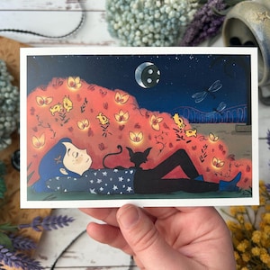 May include: A whimsical art print depicts a person with blue hair and a starry shirt, lying beneath a night sky with a crescent moon and fireflies. A black cat rests beside them. The illustration features a vibrant color palette and a dreamlike quality.