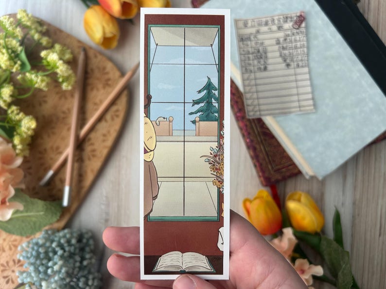 May include: A rectangular bookmark featuring an illustration of a window with a view of a tree and sky. The bookmark also depicts a person, a book, and a table. The color palette includes brown, blue, and beige.