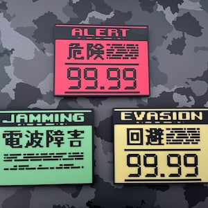 以下が含まれることがあります： 日本語と数字が書かれた白黒の四角い警告サインが3つ。 上のサインは赤で「ALERT 危険警報 99.99」と書かれている。 真ん中のサインは緑で「JAMMING 電波障害」と書かれている。 下のサインは黄色で「EVASION 回避警報 99.99」と書かれている。