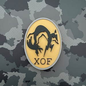 May include: A gold and gray circular patch with a black silhouette of a fox with lightning bolts and the text "XOX" in black.