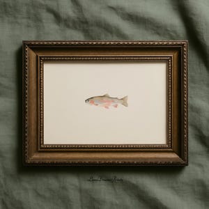 May include: A framed watercolor print of a rainbow trout. The fish is depicted in shades of pink, red, and silver, set against a cream-colored background. The frame is a dark brown with ornate detailing. The print is signed "Luna Dream Prints".