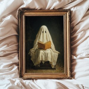 May include: A framed oil painting depicting a figure draped in a white sheet, resembling a ghost, sitting and reading an open tan book. The artwork is enclosed in an ornate, metallic gold-toned rectangular frame with intricate carved detailing.
