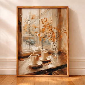 May include: A framed wall art print depicting a window view with two white ceramic coffee mugs on saucers, a clear glass vase containing orange autumn leaves, and a street scene with a car and lamp post visible through the glass pane.