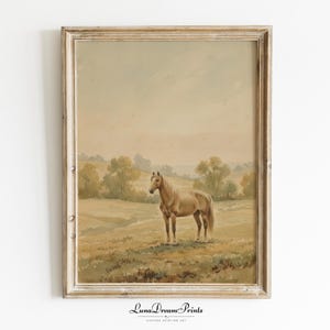 May include: A framed vintage watercolour painting depicting a horse in a field. The horse is light brown with a flowing mane and tail. The landscape features rolling hills, trees, and a muted colour palette of beige, brown, and green. The frame is a distressed, light-coloured wood. The text "Luna Dream Prints" is at the bottom.