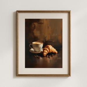 May include: A framed print featuring a still life of a cup of coffee with foam, a croissant, and scattered coffee beans. The artwork has a warm, brown color palette and a soft, painterly style, evoking a cozy cafe atmosphere.
