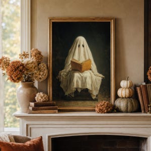 May include: A framed wall art print featuring a figure draped in a white sheet, resembling a ghost, sitting and reading an open book. The artwork is displayed on a mantelpiece alongside a ceramic vase with dried flowers and stacked pumpkins.