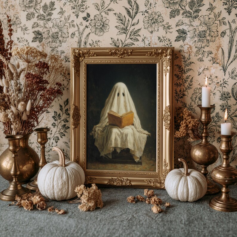May include: A framed painting of a ghost draped in a white sheet reading an open book, displayed in an ornate gold frame. The scene includes two white pumpkins, two brass candlesticks with white candles, and a brass vase with dried flowers.