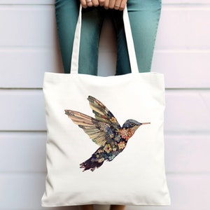May include: A white tote bag with a colorful hummingbird design. The hummingbird is made up of flowers and leaves.