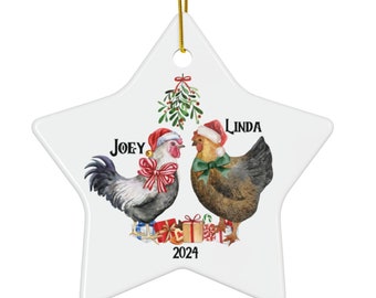 May include: A white ceramic star-shaped Christmas ornament with a red and green mistletoe design. Two chickens wearing Santa hats are under the mistletoe. The chickens are labeled "Joey" and "Linda". The ornament also includes the year "2024".