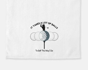 May include: White towel with a black and white illustration of a golfer standing on a tee with four golf balls. The text reads "It takes a lot of balls to golf the way I do."
