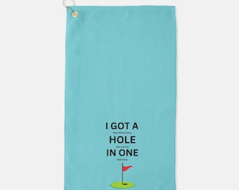 May include: A light blue golf towel with the text "I got a hole in one" and a red golf flag on a green circle.