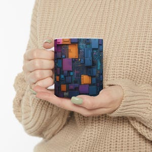 Könnte beinhalten: Eine weiße Keramiktasse mit einem farbenfrohen abstrakten Design aus Quadraten und Rechtecken in Blautönen, Lila, Orange und Rosa. Das Design ähnelt einer Leiterplatte.