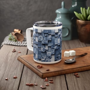 May include: A white ceramic travel mug with a blue and gray geometric pattern. The mug has a lid and a handle.