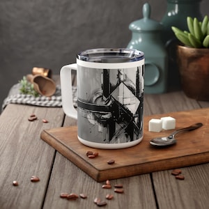 May include: A white ceramic mug with a black and white abstract design. The mug has a black handle and a silver lid.