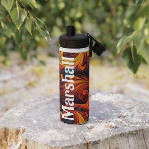 May include: A stainless steel water bottle with a black lid and a white band. The bottle features a swirling orange, yellow, and dark blue pattern with the name "Marshall" printed vertically in white.