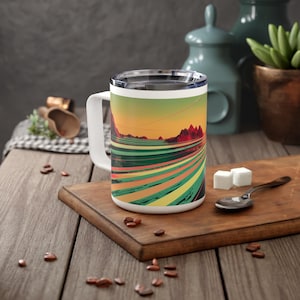 Op de afbeelding: Witte keramische reistop met een kleurrijk abstract landschapsontwerp. De mok heeft een deksel en een handvat.