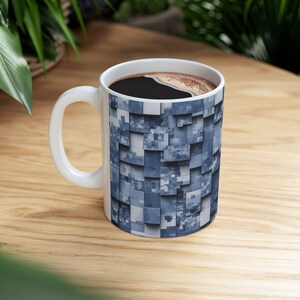 Könnte beinhalten: Eine weiße Keramik-Kaffeetasse mit einem blauen und grauen geometrischen Muster. Die Tasse ist mit Kaffee gefüllt und steht auf einem Holztisch.