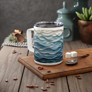 May include: White ceramic mug with a blue and white wave pattern. The mug has a handle and a lid.
