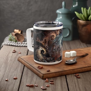 May include: White ceramic mug with a black, brown, and blue abstract design featuring swirling patterns. The mug has a handle and a lid.