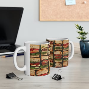 May include: Two white ceramic mugs with a pattern of colorful sandwiches on a wooden table. The mugs are filled with a white liquid.