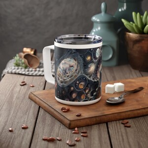 May include: A white ceramic mug with a black handle and a colorful abstract design of swirling galaxies and nebulae. The mug is sitting on a wooden surface.