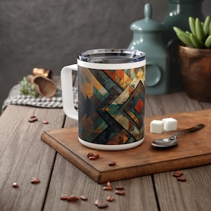Pode incluir: Caneca de cerâmica branca com um padrão geométrico em tons de marrom, azul, amarelo e vermelho. O padrão lembra a arte indígena americana.