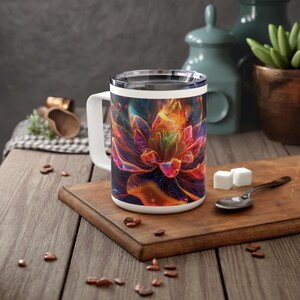 May include: A white ceramic mug with a colorful abstract flower design. The mug has a black handle and a stainless steel lid.