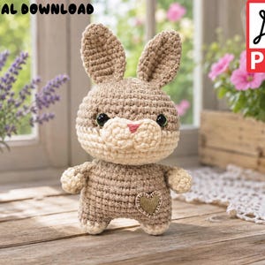 May include: A crochet bunny toy featuring light brown and cream yarn, black plastic eyes, a pink stitched nose, and a small gold heart patch on the chest. The image includes the text DIGITAL DOWNLOAD and a PDF icon, indicating a digital pattern file.