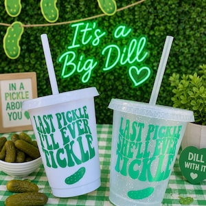 May include: Two reusable plastic tumblers with lids and straws. One cup is solid white, the other is clear with glitter. Both feature green text reading "LAST PICKLE I'LL EVER TICKLE" or "LAST PICKLE SHE'LL EVER TICKLE" and a small green pickle graphic.