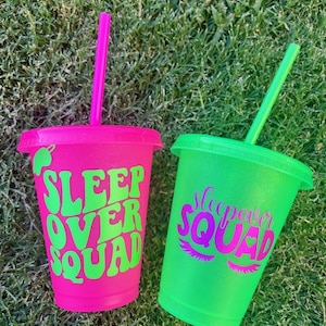 K&ouml;nnte beinhalten: Zwei glitzernde Plastikbecher mit Strohhalmen. Einer ist leuchtend rosa mit den Worten "SLEEP OVER SQUAD" in Gr&uuml;n. Der andere ist gr&uuml;n mit den Worten "Sleepover SQUAD" in Pink. Beide Becher stehen auf gr&uuml;nem Gras.