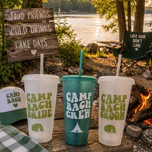 May include: Three plastic tumblers with lids and straws. Two are frosted white with green text reading Camp Bach Bride and Camp Bach Groom with camper icons. The center tumbler is glittery green with white text reading Camp Bach Crew and a tent icon.