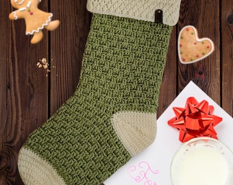 May include: A green and white crocheted Christmas stocking with a white cuff and a brown leather loop. The stocking is hanging on a wooden surface.