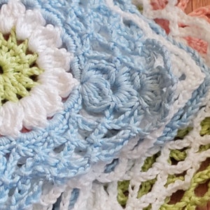 May include: Close-up of a crocheted blanket with a light blue, white, and green color scheme. The blanket is made of multiple squares with different patterns.