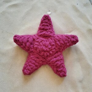 May include: A plush pink starfish shaped pillow. The pillow is made of a soft, fuzzy material and is perfect for cuddling.