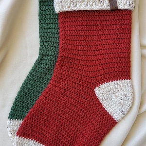 Può includere: Un calzino di Natale lavorato a uncinetto rosso, verde e bianco con un'etichetta in pelle marrone che dice "Buona fortuna" appesa in alto.