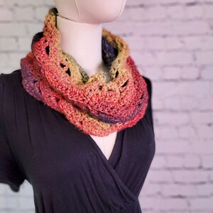 May include: A crocheted cowl in shades of red, orange, yellow, and blue. The cowl is worn by a mannequin with a black dress.