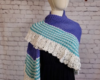 May include: A handmade shawl in shades of periwinkle, turquoise, and white. The shawl features a knitted design with a scalloped edge. The color scheme is a mix of solid and patterned sections, creating a visually appealing accessory.