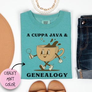 Peut inclure: Un t-shirt bleu turquoise avec le texte "A Cuppa Java & Genealogy" et une tasse de café de dessin animé tenant une loupe. La tasse de café a un visage heureux et marche. Le texte est en noir et la tasse de café est marron.