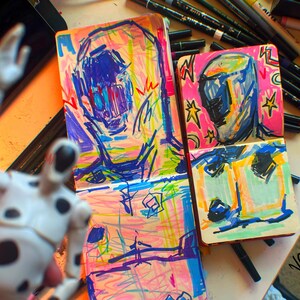 Pu&ograve; includere: Due quaderni da schizzo aperti con disegni colorati di figure astratte. I disegni sono realizzati in colori vivaci, tra cui rosa, blu, verde, giallo e arancione. I quaderni da schizzo sono su una superficie bianca con una variet&agrave; di pennarelli colorati.