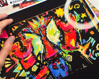 May include: A vibrant, abstract art print with a black border. The artwork features bold strokes of red, yellow, blue, and green, creating a dynamic and colorful composition. The print is held by a hand, with a shop sticker in the background.