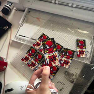 Puede incluir: Una colecci&oacute;n de pegatinas coloridas con un personaje de superh&eacute;roe de dibujos animados con un traje rojo y azul. Las pegatinas est&aacute;n impresas en papel blanco y tienen un contorno negro. Las pegatinas est&aacute;n dispuestas en un patr&oacute;n de cuadr&iacute;cula.