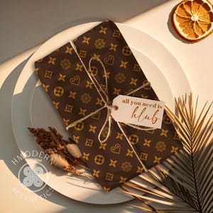 May include: A brown gift box with a gold pattern and a white gift tag that says "all you need is klub". The box is on a white plate with a brown background.