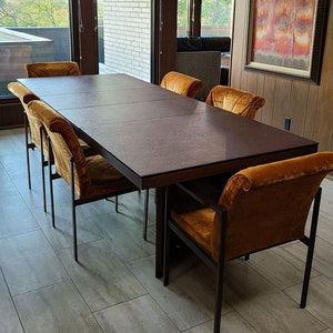 May include: A dark brown rectangular dining table with a leather top and a black metal frame. Six mustard yellow chairs with black metal frames surround the table.