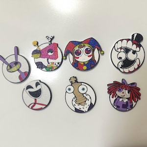 Peut inclure: Un ensemble de sept épinglettes circulaires présentant des illustrations de personnages de dessins animés colorés. Les motifs incluent une créature aux oreilles violettes, une forme géométrique, un bouffon, un visage souriant et une poupée.