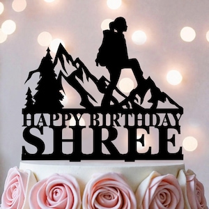 May include: Black cake topper with a mountain range and a hiker silhouette. The text "HAPPY BIRTHDAY SHREE" is displayed in bold letters. The cake is decorated with pink roses.